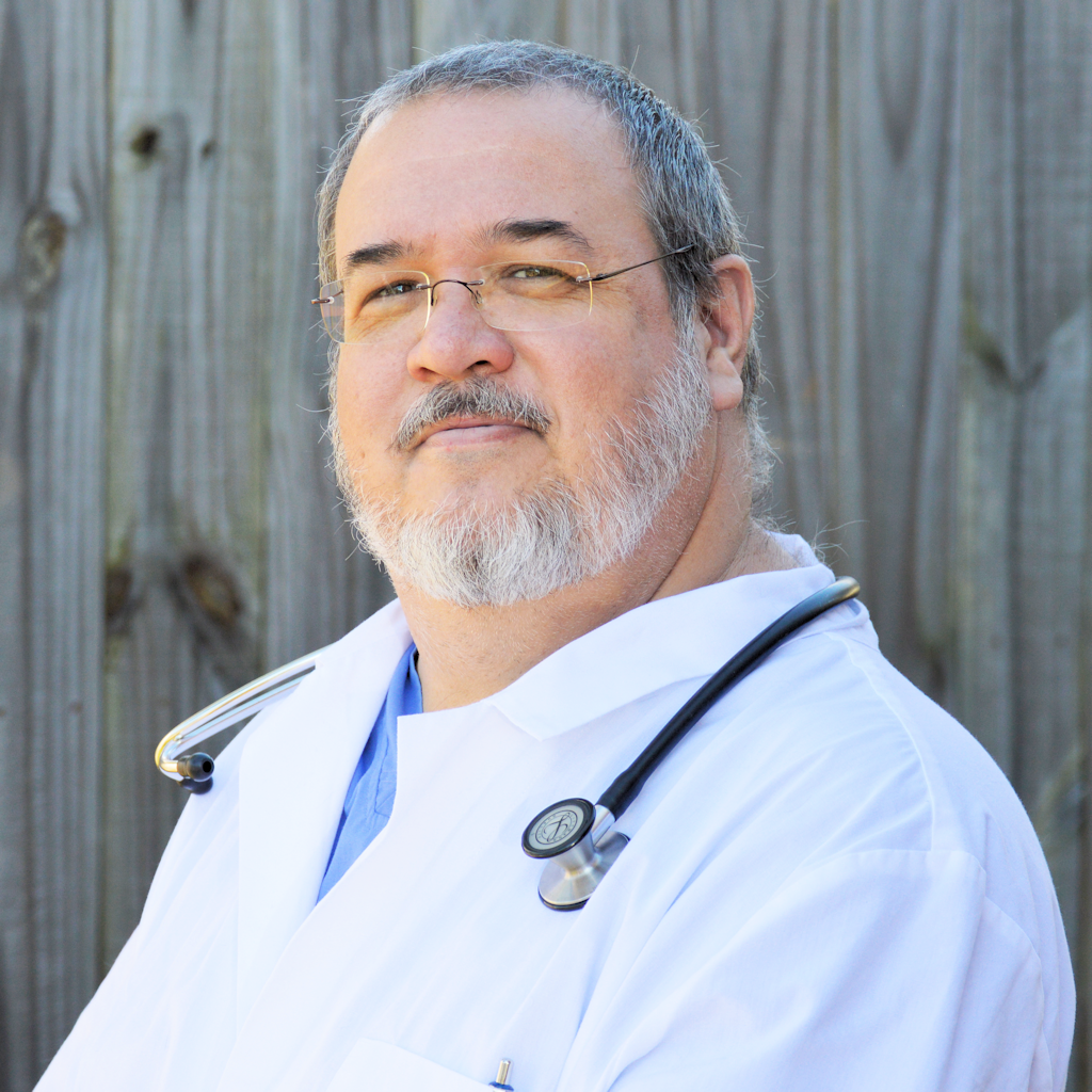 Headshot of a bearded Veterinarian wearing a stethoscope and white coat, smiling warmly.