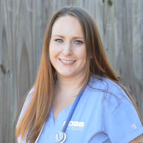 Headshot of a smiling veterinary technician with long red hair wearing seal blue scrubs.